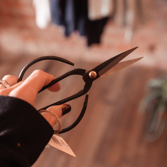 Hand holding a pair of black-handled scissors with a blurred background