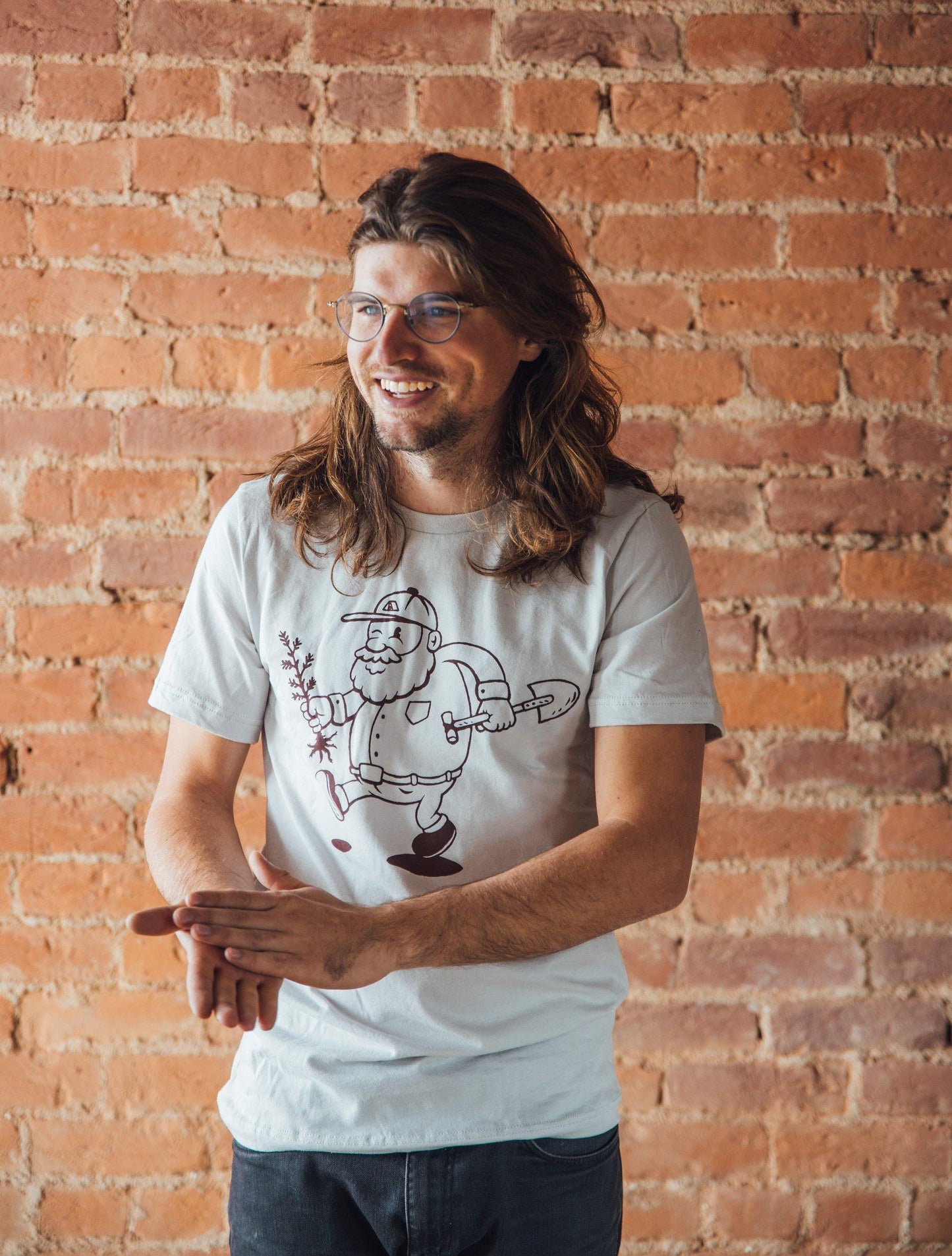 Man wearing grey tee shirt picturing a man planting a tree. Outdoor mountain style