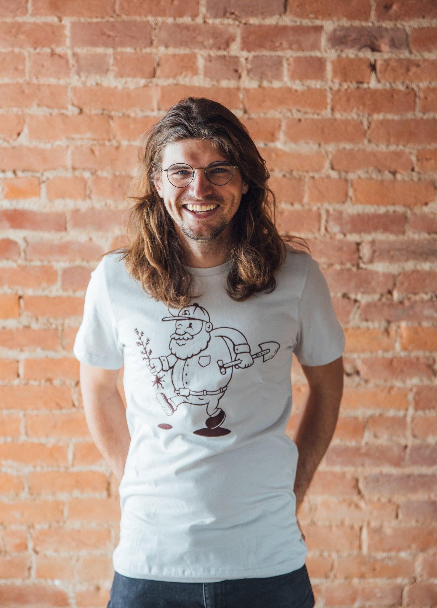Man wearing grey tee shirt picturing a man planting a tree. Outdoor mountain style