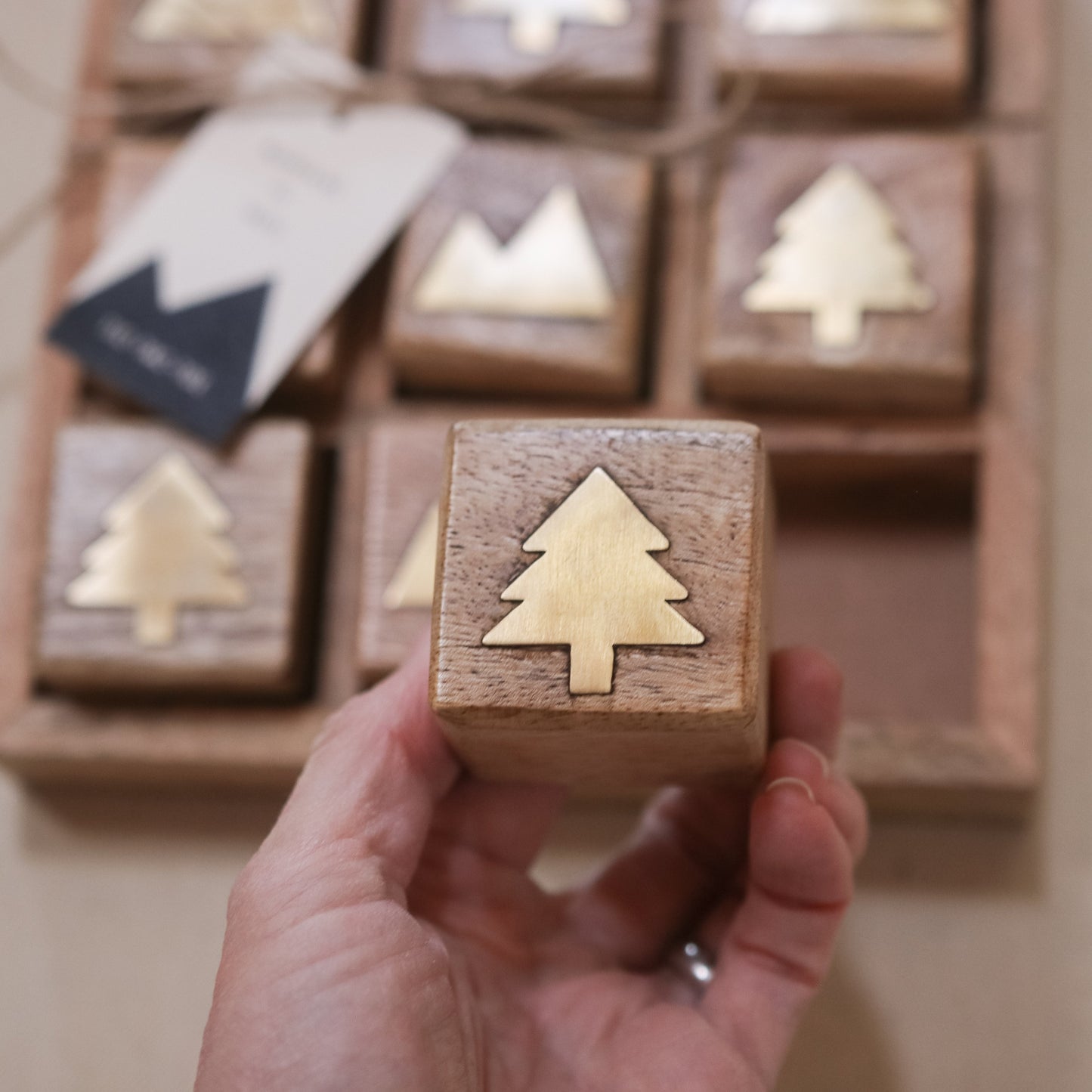Hand holding a wooden block with a tree design in front of a advent calendar.