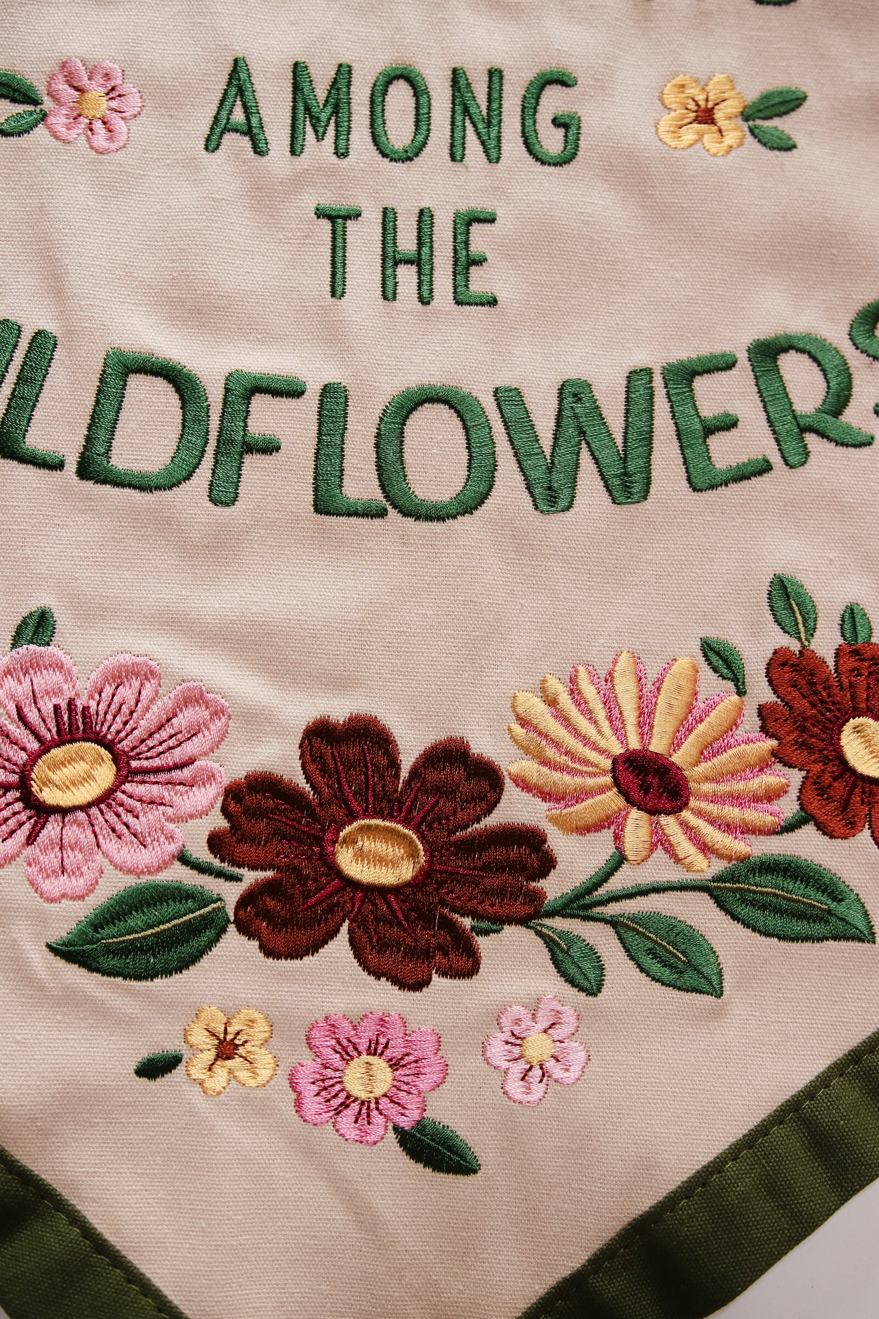 Embroidered text 'AMONG THE WILDFLOWERS' with floral designs on a beige background