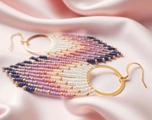 Beaded earrings with gold hooks on a soft pink fabric background