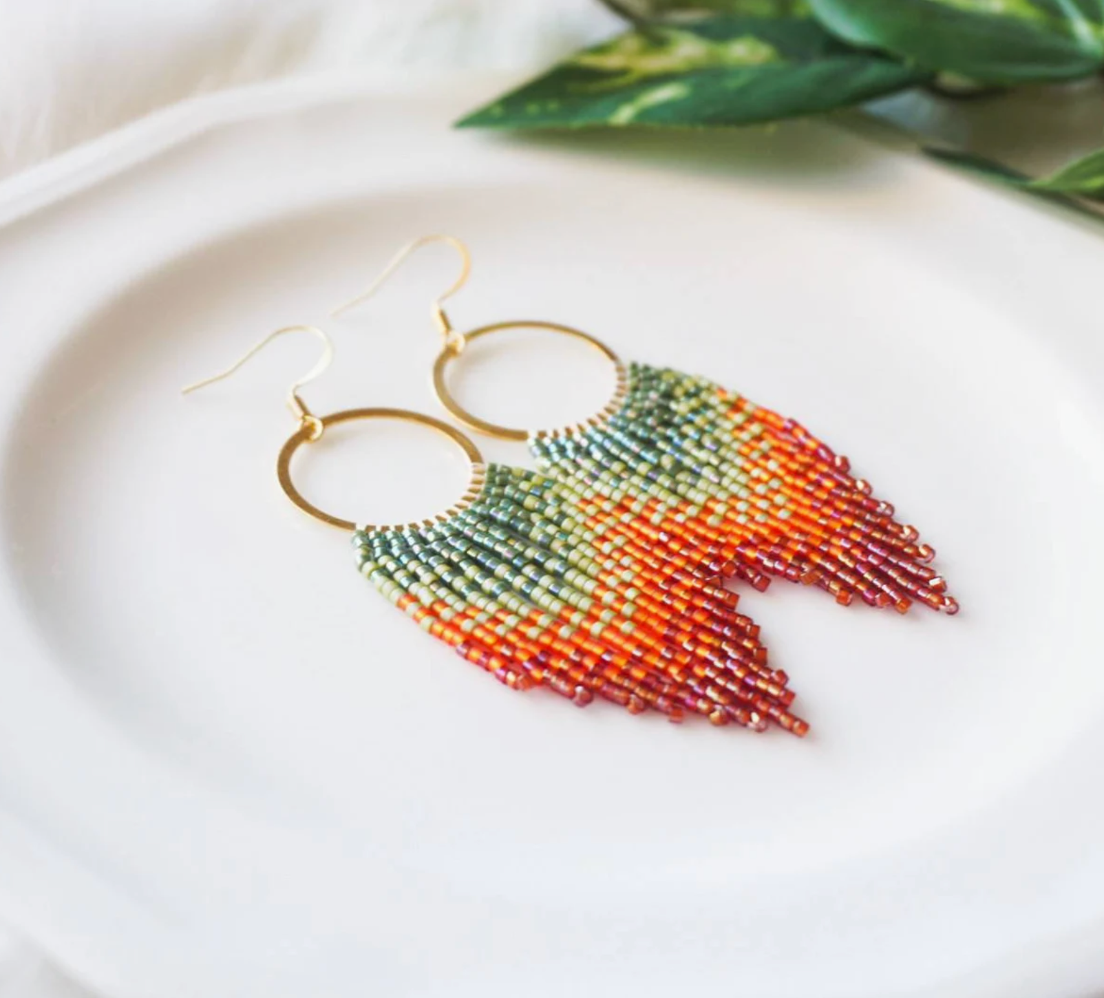 Beaded earrings with a gold hoop on a white surface with green leaves in the background
