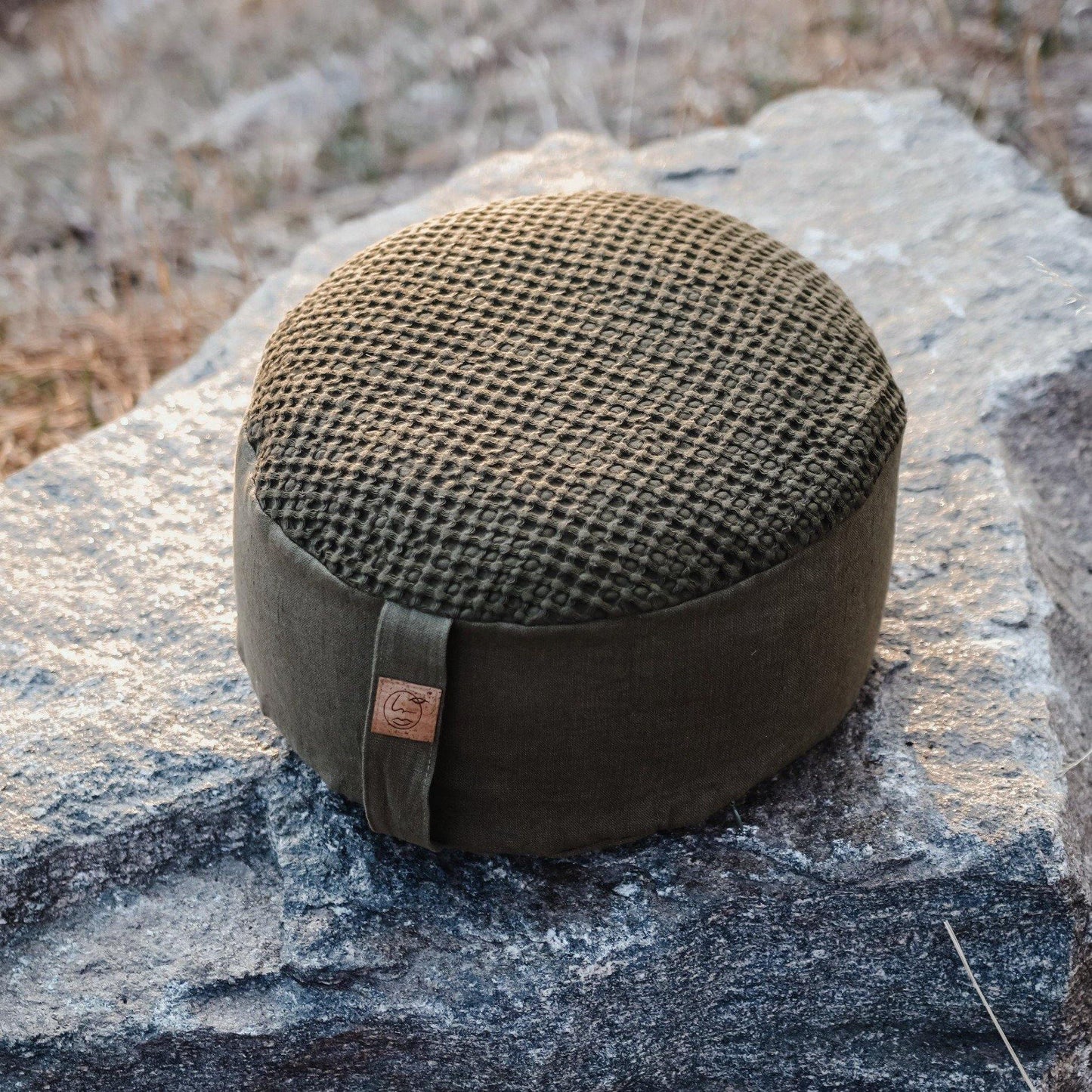 Olive colored waffle and linen zafu meditation cushion on a rock