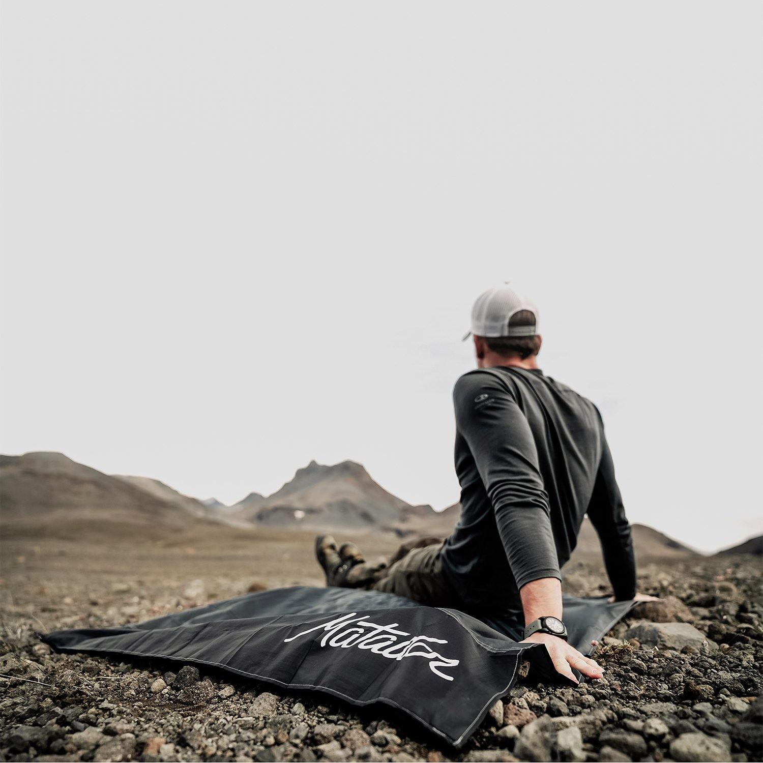 Man sitting on Black waterproof packable pocket blanket or ground cover in the mountains