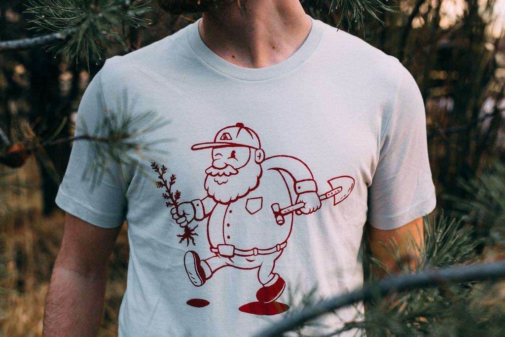 Man wearing grey tee shirt picturing a man planting a tree. Outdoor mountain style