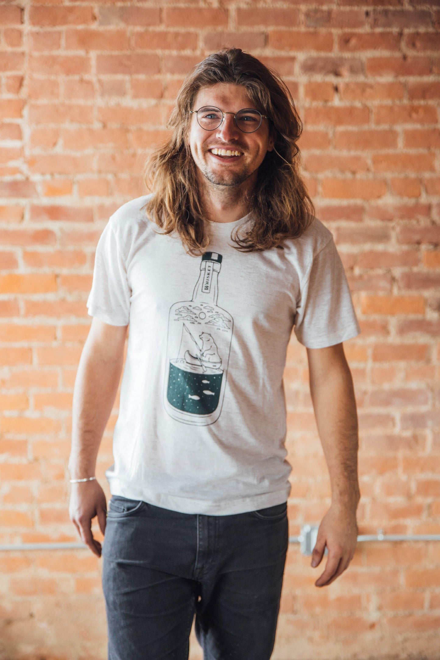 Man wearing a Oatmeal colored shirt picturing a whiskey bottle and a bear fishing