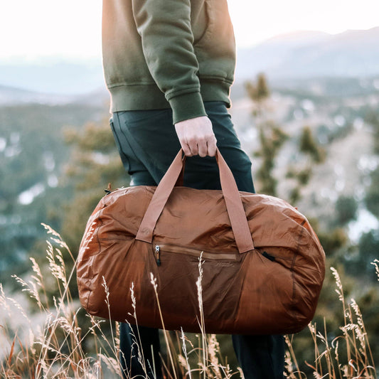 Man carrying brown waterproof packable duffle bag in the mountains